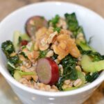 A salad of cooked farro, sliced red grapes and celery with kale look beautiful in a plain white bowl.