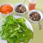 Dishes of grated carrot, tofu vegetable filling, sauce and lettuce leaves.