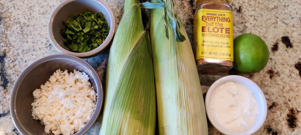 Elote ingredients: greek yoghurt mayonnaise mixture, ears of corn, queso fresco, cilantro, spices and lime.