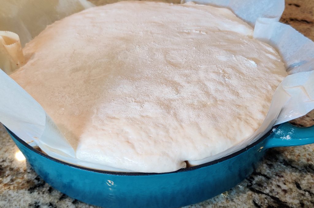 Sourdough bread rising in parchment paper in a baking pan on the counter.