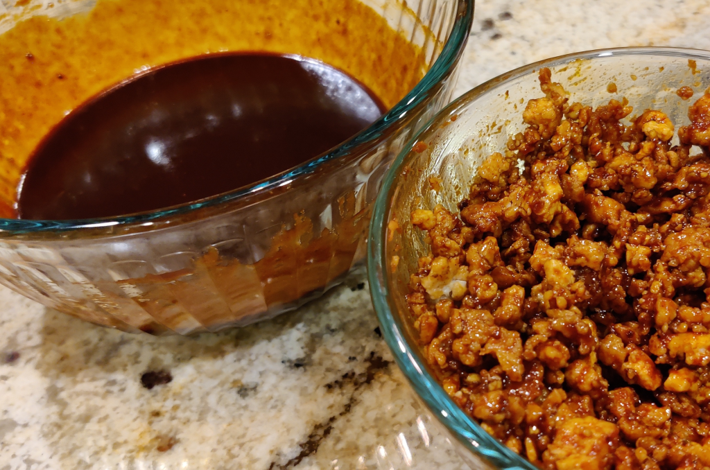 Sweet, spicy and umami Gochujang sauce in a glass mixing bowl being stirred into sautéed tofu.