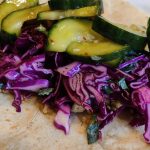 Flour tortillas topped with tofu in a gochujaru sauce, purple cabbage slaw and Korean pickled cucumbers.