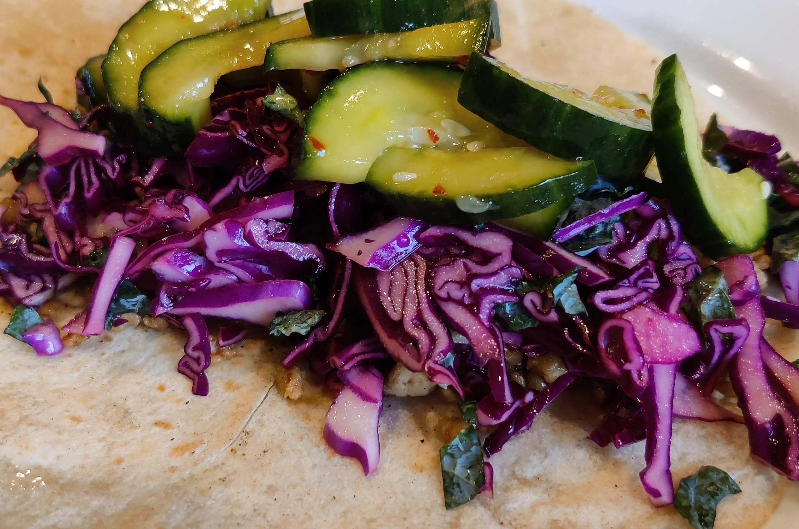 Flour tortillas topped with tofu in a gochujaru sauce, purple cabbage slaw and Korean pickled cucumbers.
