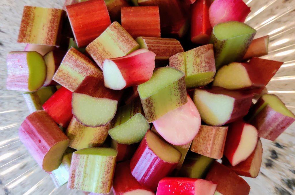 Bright pink and green stalks of fresh rhubarb cut into half inch pieces in a glass bowl.