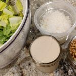 Romaine lettuce, caesar salad dressing, grated parmesan and toasted breadcrumbs on the counter.