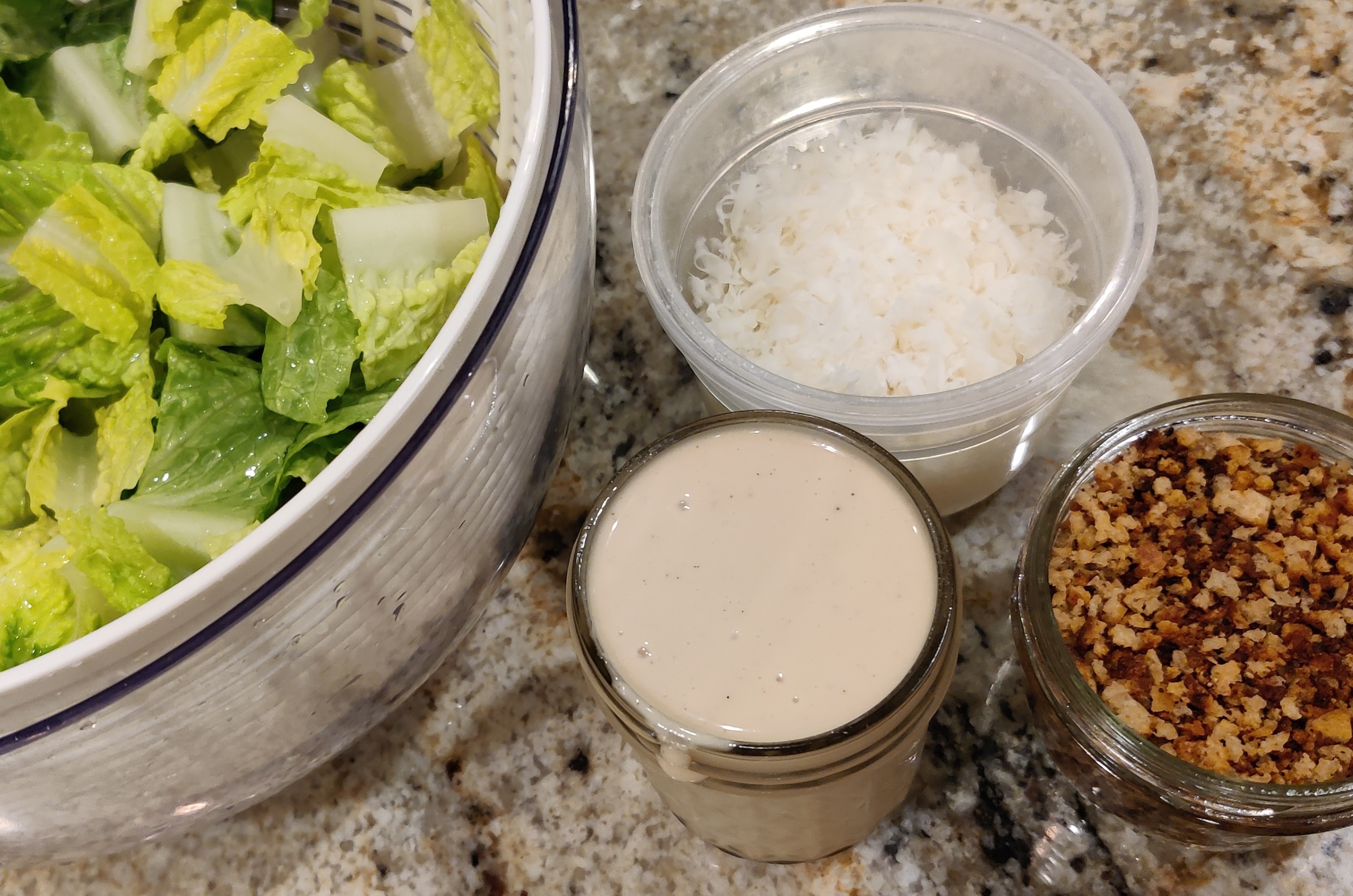 Romaine lettuce, caesar salad dressing, grated parmesan and toasted breadcrumbs on the counter.