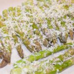 Asparagus spears on a baking sheet topped with freshly grated parmesan.
