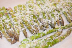 Asparagus spears on a baking sheet topped with freshly grated parmesan.