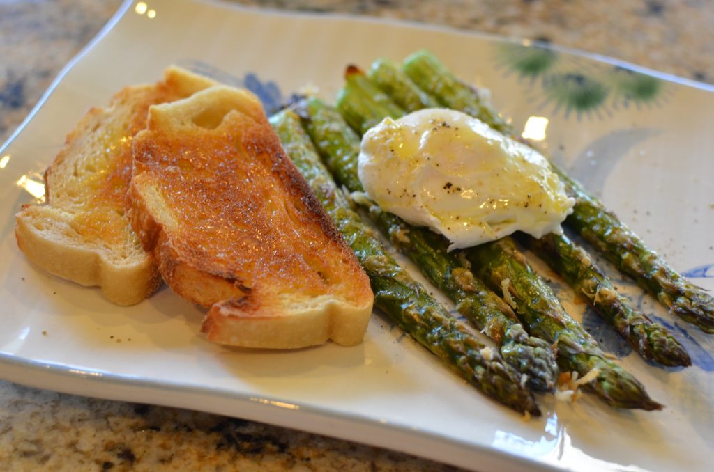 Roasted asparagus topped with a poached egg next to a slice of toast on a plate.