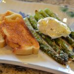 Roasted asparagus topped with a poached egg next to a slice of toast on a plate.