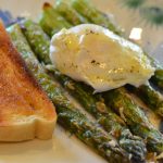 Roasted asparagus topped with a poached egg on a plate next to a slice of buttered sourdough toast.