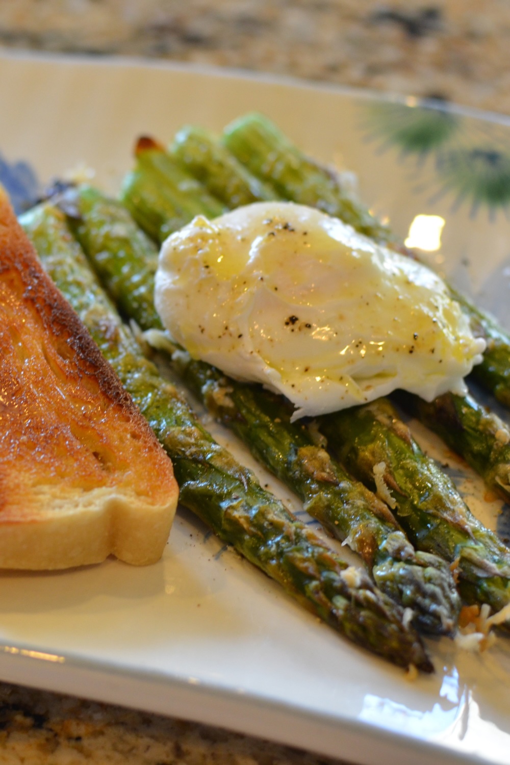 Roasted asparagus topped with a poached egg on a plate next to a slice of buttered sourdough toast.