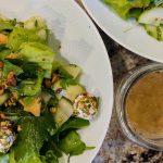 Fresh green salad in a bowl next to a jar of homemade vinaigrette salad dressing.