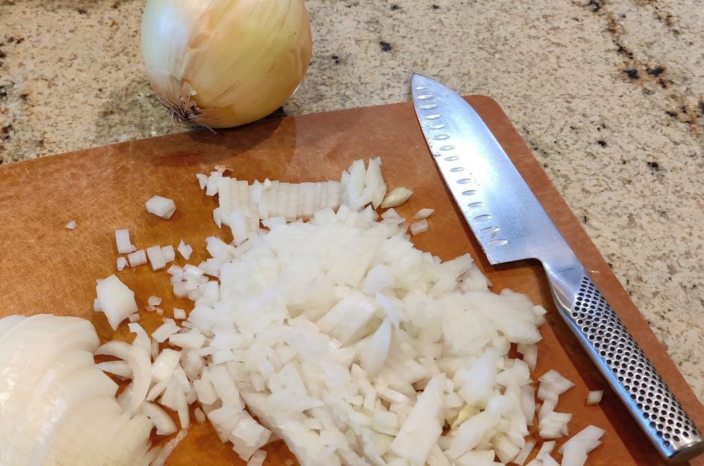 Cutting board with chef knife and diced onions.