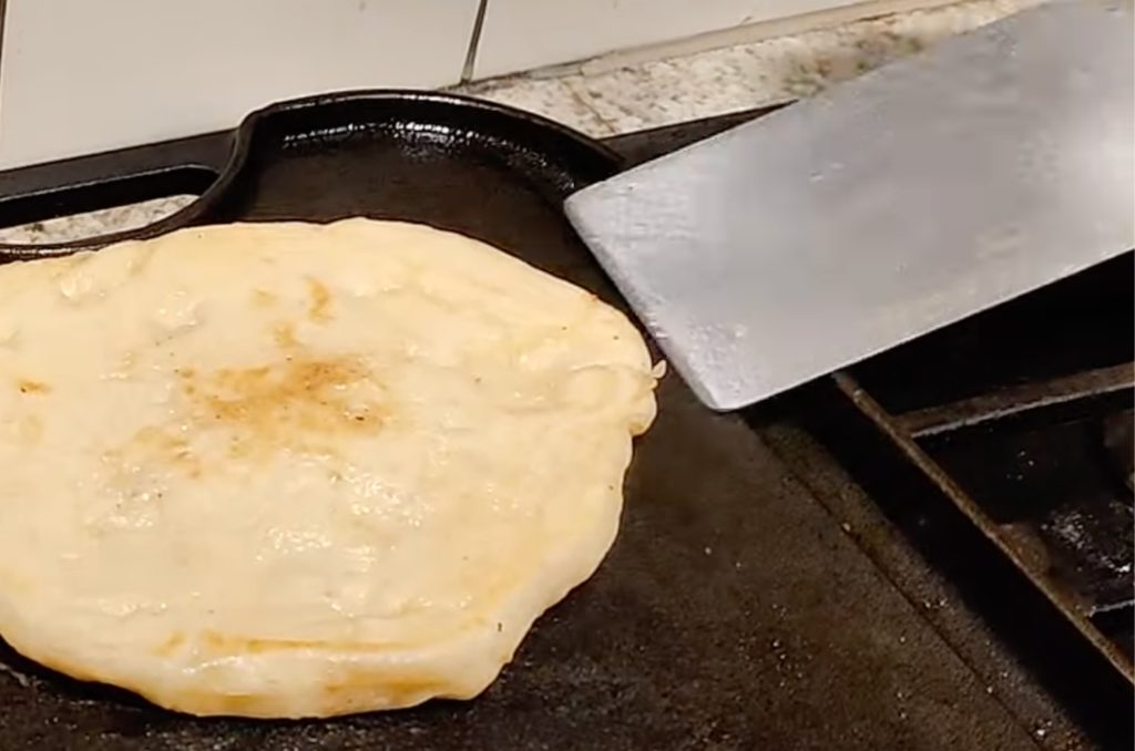 Metal spatula flipping flat bread on a griddle.